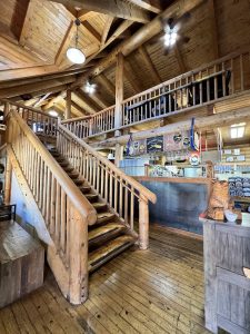 Rustic lodge interior in Arches National Park featuring a wide wooden staircase, log beams, and a dim bar area.