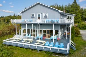 Blue two-story lodge with a wraparound deck sits among pines at Acadia National Park.