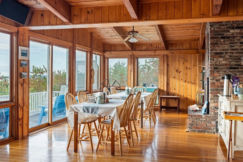 A sunlit wood-paneled lodge dining room in Acadia National Park, with large windows and a brick fireplace.