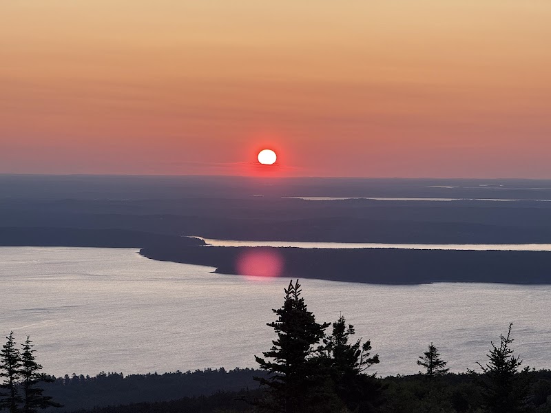Cadillac Mountain Overlook at sunset over the water and forested shoreline in Acadia National Park.
