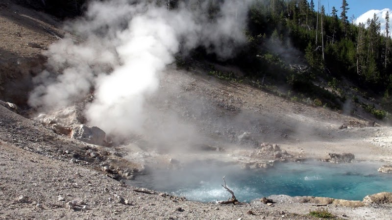 Firehole River along Yellowstone National Park shows a steaming, turquoise pool amid rocky terrain.