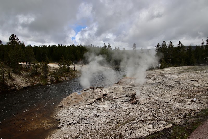 Steam vents rise from rocky ground beside the Firehole River in Yellowstone National Park, a geothermal feature along the riverbank.