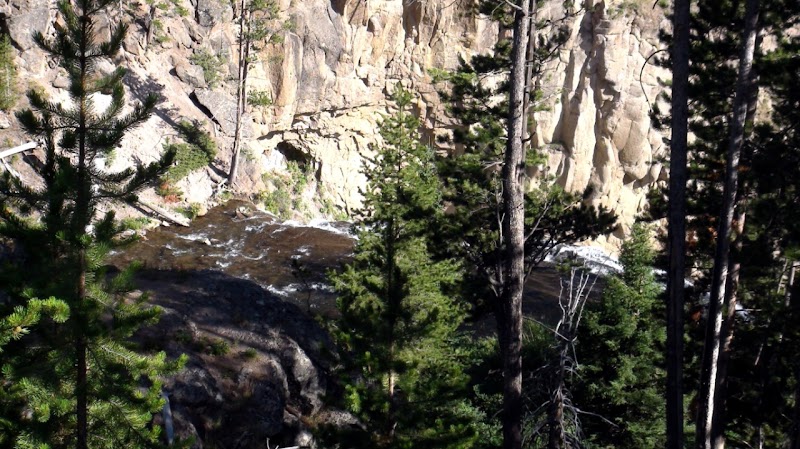 Firehole River winds through pines and rocky cliffs in Yellowstone National Park, a scenic canyon view.