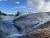 Firehole River winds along steaming geothermal banks in Yellowstone National Park, with blue sky and trees in the background.