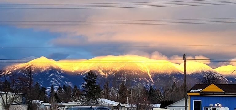 Glacier National Park snow-capped peaks glow at sunset behind a small town gift shop.