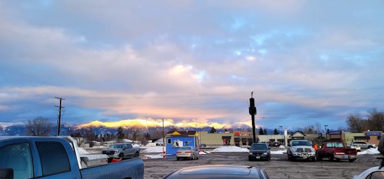 Surplus gift shop storefronts near Glacier National Park town center at sunset with snow visible on the ground.