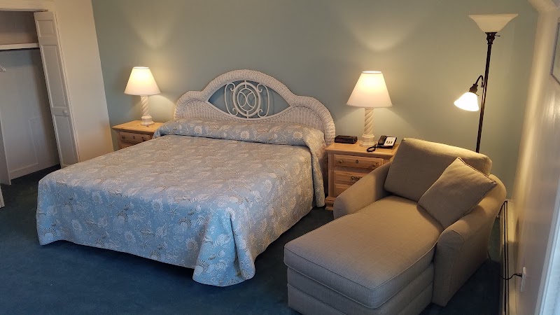 Cozy Acadia National Park lodging bedroom with blue duvet, wicker headboard, two lamps on nightstands, and a beige chair.