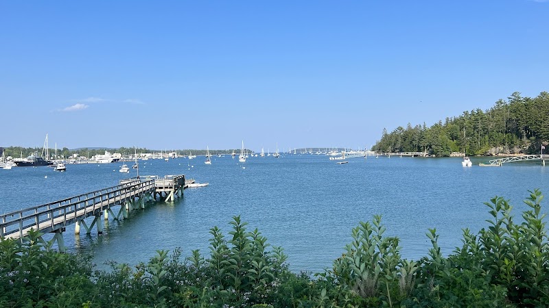Sailboats and small boats dot a calm harbor at Acadia National Park, with a wooden pier stretching into blue water.