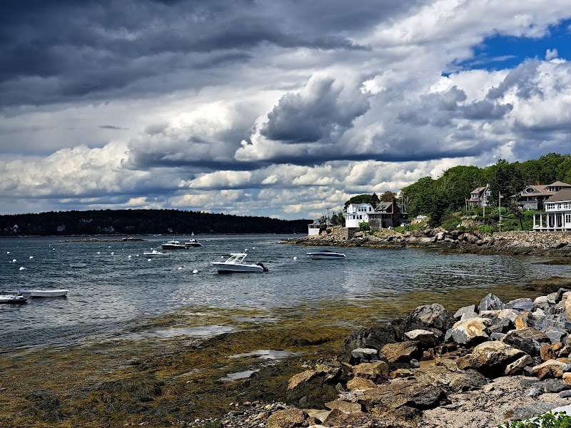 Boats anchored in a rocky cove near Southwest Harbor, with hillside houses and a dramatic clouded sky in Acadia National Park.