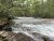 Johns Lake Loop Trailhead winds along a fast-flowing river with rocky ledges and dense forested banks in Glacier National Park.