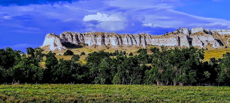 Wide view of white limestone cliffs along a rugged ridge above a green forest and grassy plain at Badlands National Park.