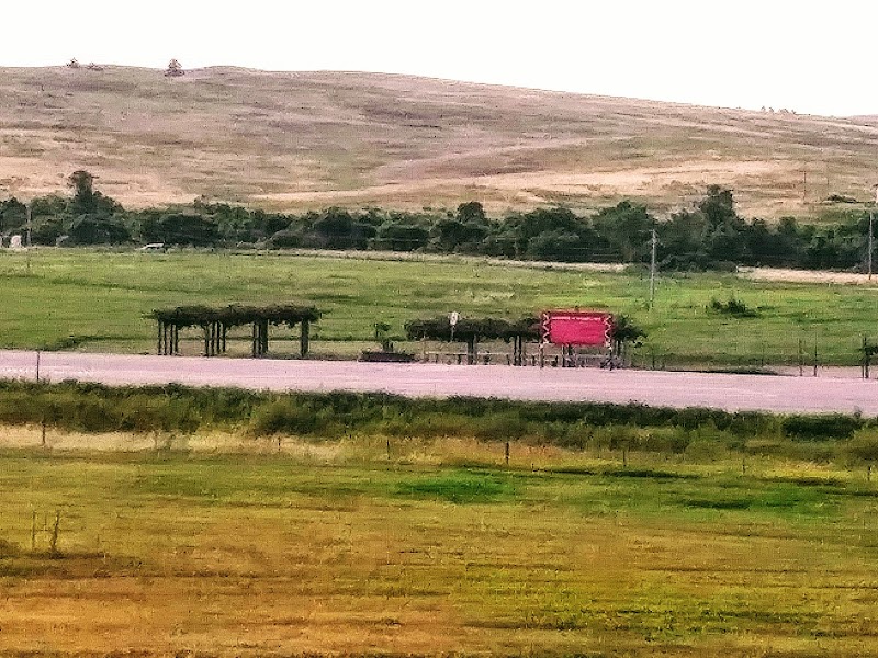 Pasture fields, a road with wooden shaded structures and a red sign, set against rolling hills in Badlands National Park.