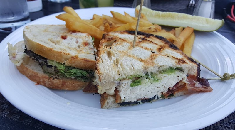 Grilled sandwich halves with greens and meat on a white plate, with fries and a pickle, in Acadia National Park.