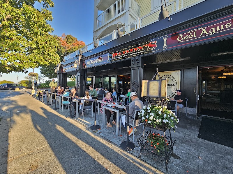 Outdoor sidewalk dining along a dark storefront with patrons at tables under a blue sky in Acadia National Park.