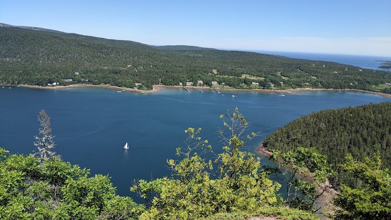 Scenic overlook from Acadia Mountain Trailhead: blue harbor, forested hills, and a lone white-sailed boat in Acadia National Park.