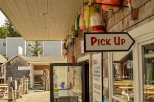 Colorful lobster buoys hang from the storefront in Acadia National Park, with a Pick Up sign and glass window counter.