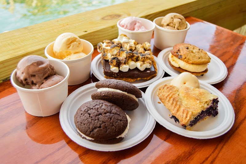 Assorted desserts on white plates and cups—ice cream, cookies, brownies, and pie on a wooden table by the water in Acadia National Park.