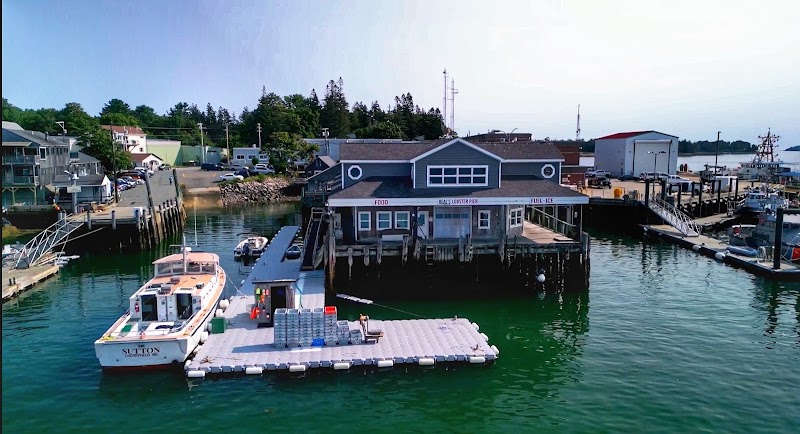 Waterfront lobster pier with a blue-gray restaurant on pilings, a docked boat, and a floating platform in Acadia National Park.