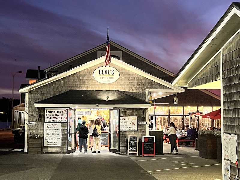 Exterior of a seaside restaurant with a pitched roof and warm lights, people waiting outside at Acadia National Park.