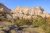 Beige cliff shelves rise above a scrubby foreground of grasses and evergreens at Badlands National Park.