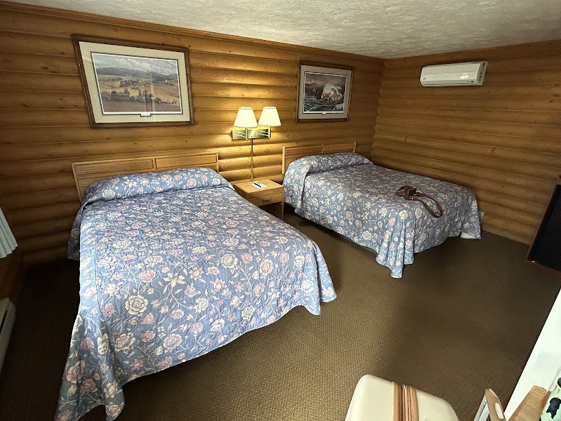 Two queen beds with blue floral quilts, wood-paneled walls, framed art, bedside lamps, and a wall AC in Yellowstone National Park.