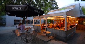 Outdoor patio with metal tables and chairs beside a glass-walled, warmly lit dining area in Acadia National Park.