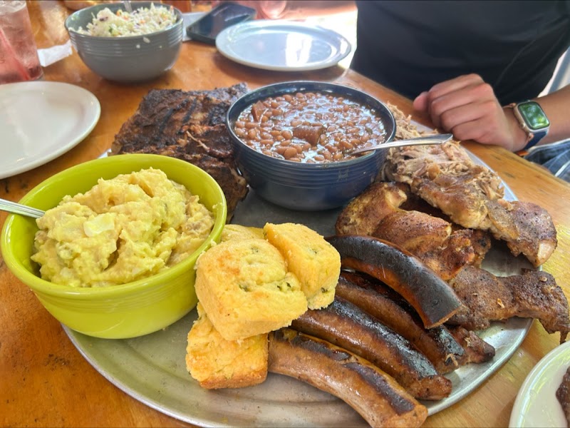 Assorted barbecue meats, ribs and sausages, baked beans, cornbread, and mashed potatoes on a metal platter at Acadia National Park.