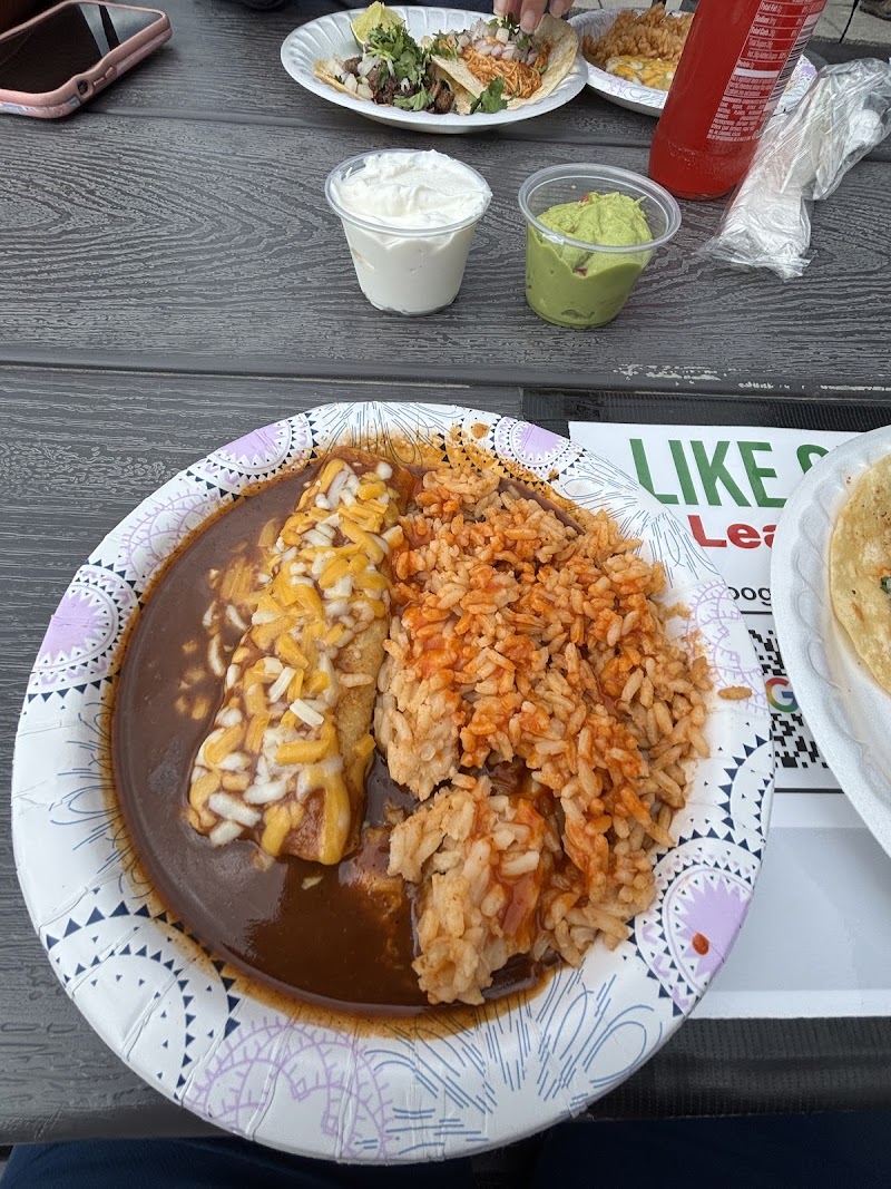 Plate with brown sauce, cheese-topped protein, onions, and orange rice, plus sour cream and guacamole cups on a wooden table in Yellowstone National Park.
