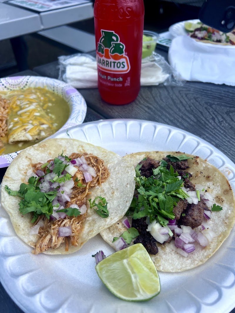 Two soft corn tortillas with shredded chicken and beef, onions, cilantro, and lime on a plate in Yellowstone National Park.