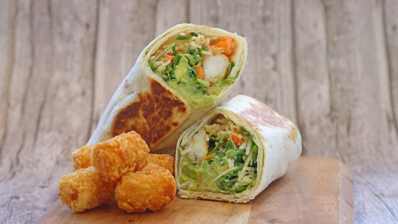 Two flour wraps filled with avocado, greens, and rice sit on a wooden board beside crispy tater tots in Yellowstone National Park.
