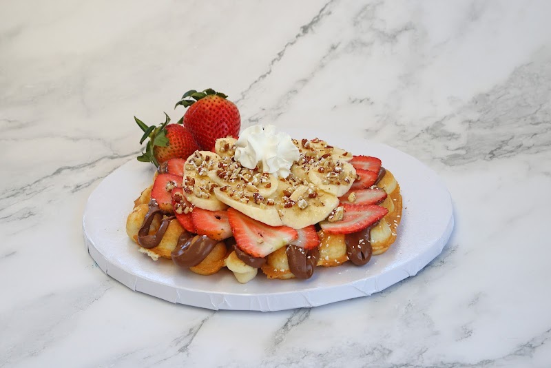 Waffle topped with bananas, strawberries, whipped cream, pecans, and chocolate drizzle on a white platter in Yellowstone NP.