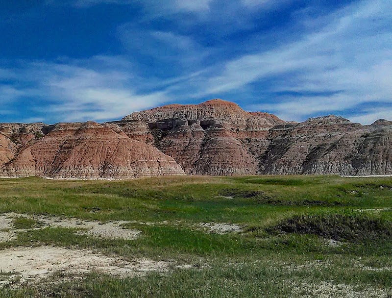 Red-banded Badlands mesas rise across a green field under a clear blue sky at Badlands National Park.