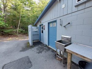 Blue-gray facility building with blue doors, a stainless sink, and a forested driveway at Acadia National Park.