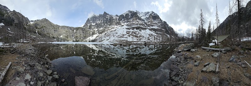 Lincoln Lake Campground sits beside a calm alpine lake with snow-capped peaks in Glacier National Park.