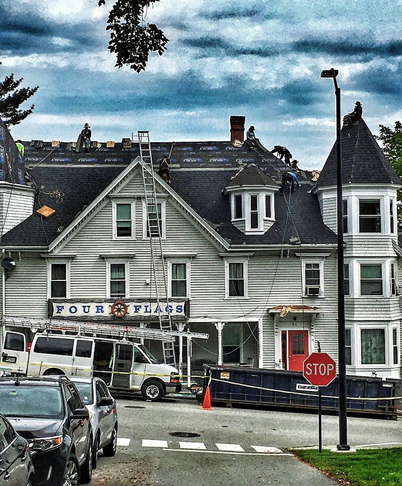 Castine town house undergoing roof renovations near Acadia National Park, with workers on the roof and a ladder.