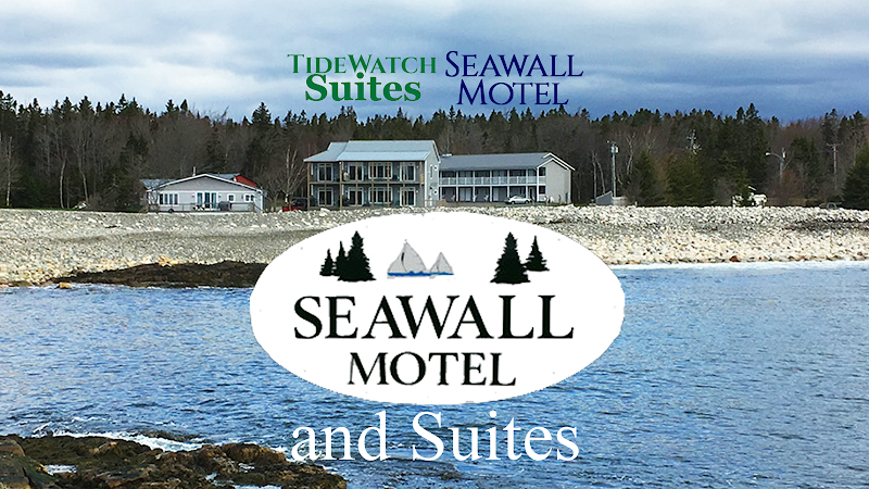 Coastal motel buildings sit along rocky shoreline with calm blue water and evergreen trees at Acadia National Park.