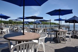 Outdoor seating at a waterfront restaurant patio in Acadia National Park with blue umbrellas and white chairs.