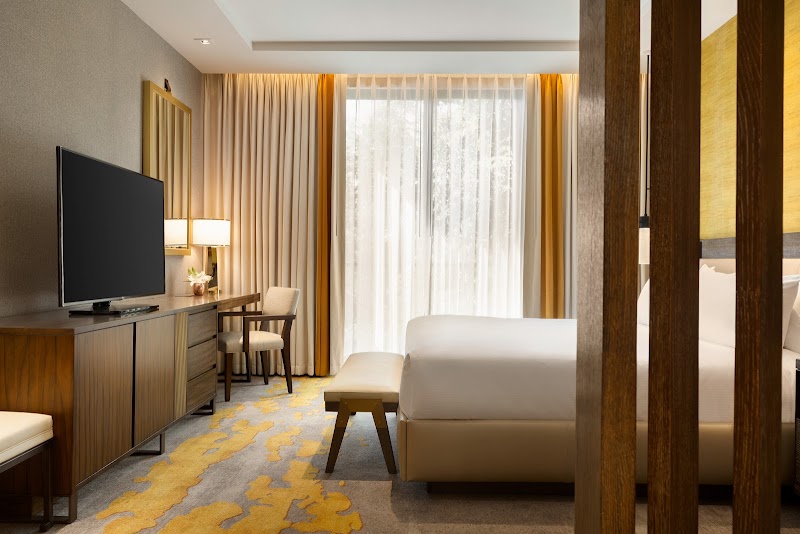 Cozy hotel room with a white king bed, wooden desk, flat-screen TV, soft bench, and sheer curtains opening to Arches National Park.