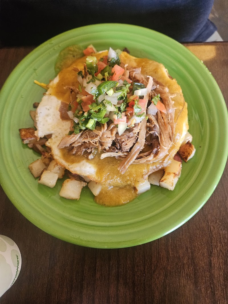 Shredded pork tostada topped with pico de gallo and cheese sauce on a crispy tortilla, with diced potatoes on a green plate in Arches National Park.