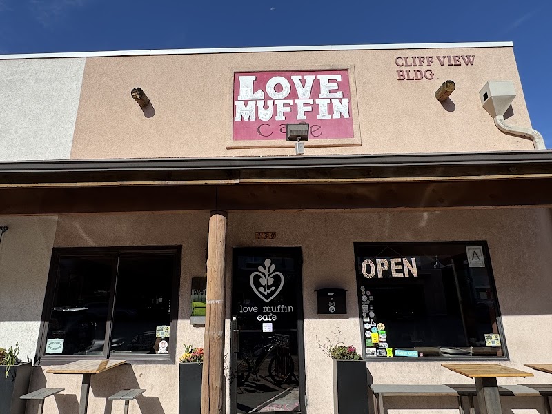 Facade of a small cafe in Arches National Park area, pink sign above the entrance, open doors, and outdoor tables.