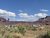 Arches National Park campground with RVs and trailers parked among shrubs, red rock mesas in the distance under a blue sky.