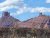 Two red sandstone mesas loom over a scrubby foreground under a bright sky at Arches National Park.