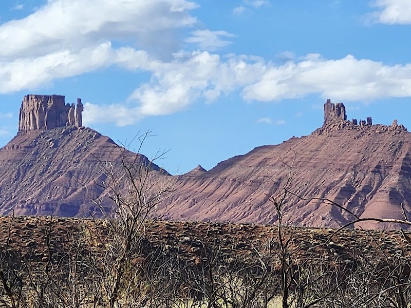 Two red sandstone mesas loom over a scrubby foreground under a bright sky at Arches National Park.