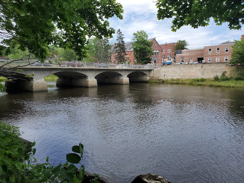 Ellsworth town bridge over a calm river near Acadia National Park, with brick buildings and green trees.