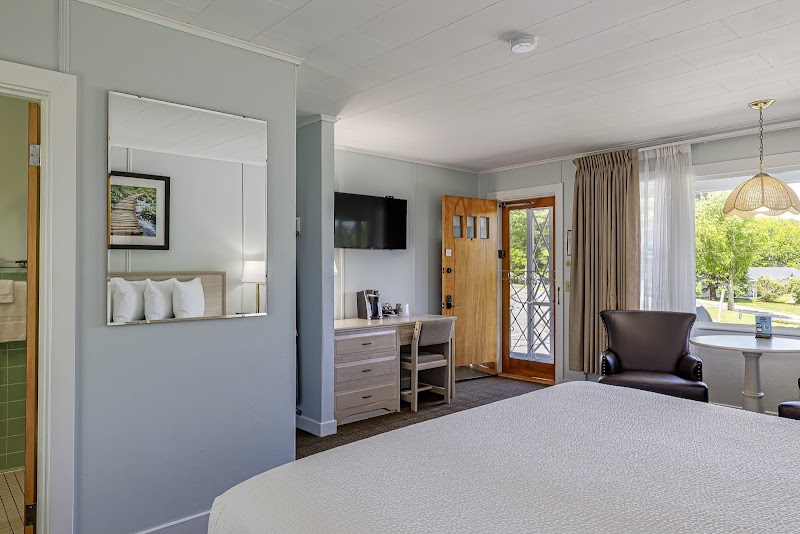 Bright hotel room in Acadia National Park with a large bed, dresser, wall mirror, desk, TV, and a seating area by the window.