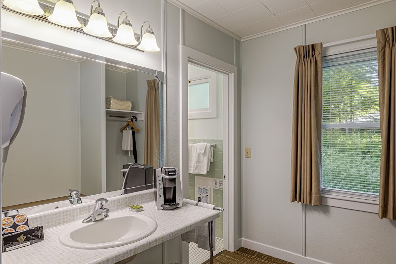 Motel bathroom in Acadia National Park with tiled counter, sink, mirror, coffee maker, towels, open closet, and a window with brown curtains.