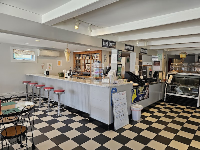 Bright white cafe interior with a long counter, red stools, and a checkered floor in Acadia National Park.