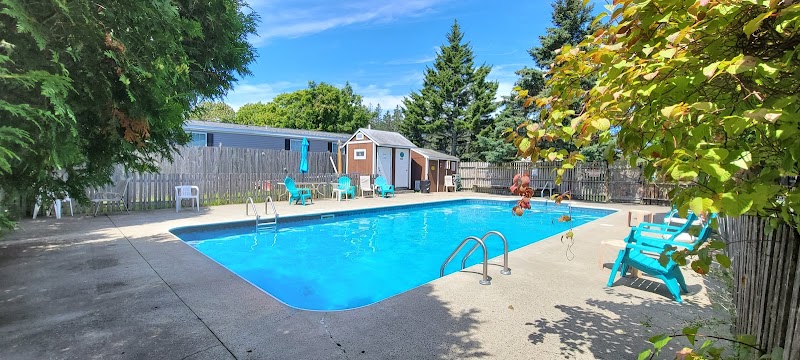 Bright blue swimming pool with a concrete deck, turquoise chairs, and wooden sheds at a campground in Acadia National Park.