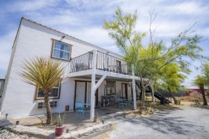 Ghost Town Hotel exterior in Big Bend National Park, a white two-story lodging with a balcony and blue chairs.