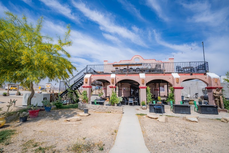 Exterior view of a two-story adobe-style lodge with arches and patio seating, near Big Bend National Park.